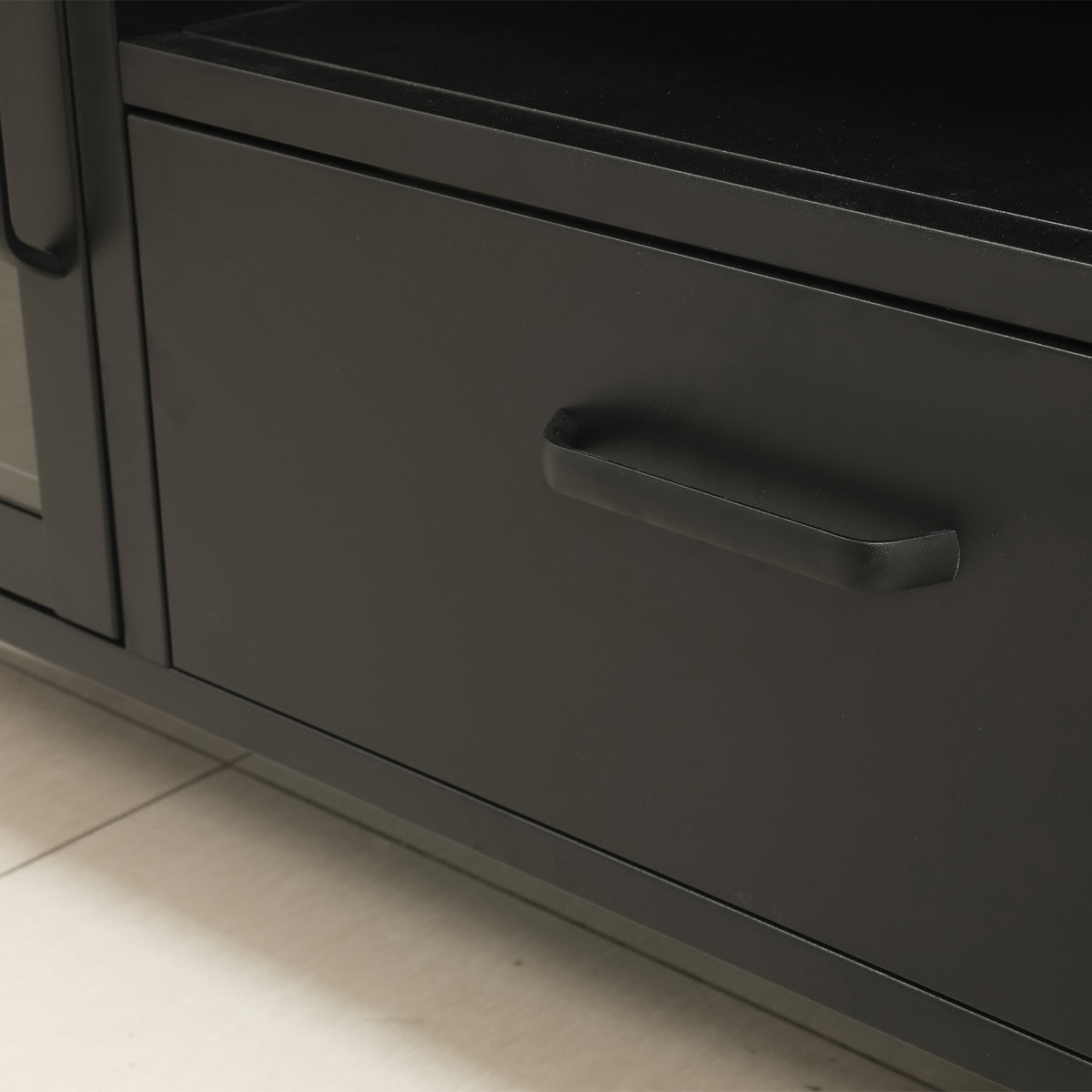 Close-up of the black TV cabinet's central drawer, highlighting the black horizontal handle and smooth finish.
