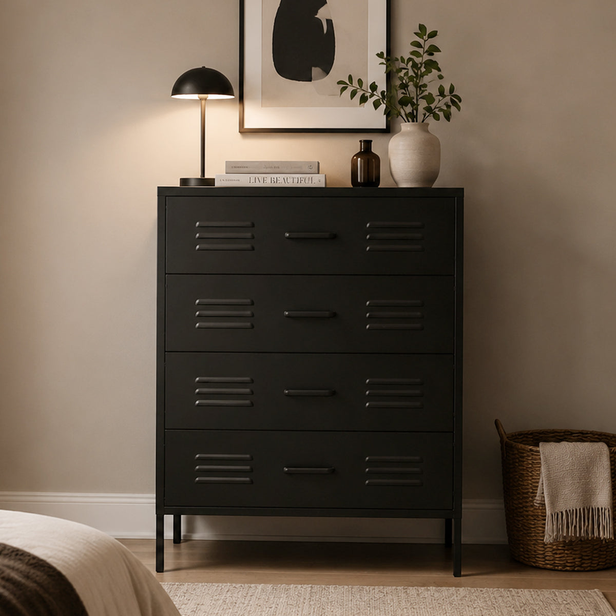 A tall black 4-drawer chest of drawers in a styled bedroom setting, topped with a black table lamp, books, a small bottle, and a white vase with greenery.