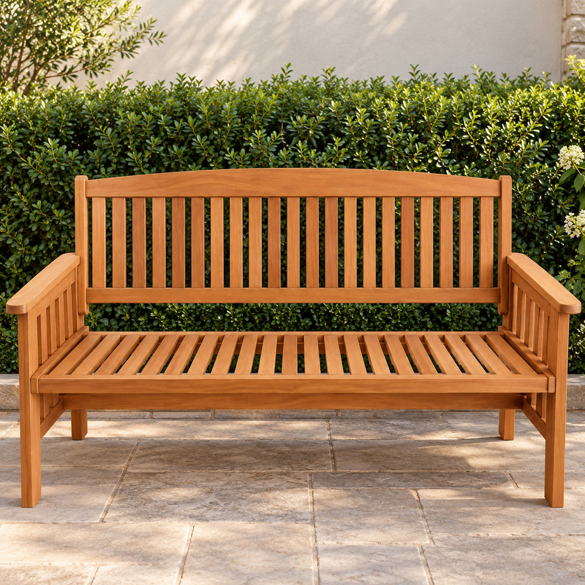 Outsidings Santos three-seater wooden bench displayed on a paved outdoor patio against a lush green hedge, highlighting its natural timber finish.