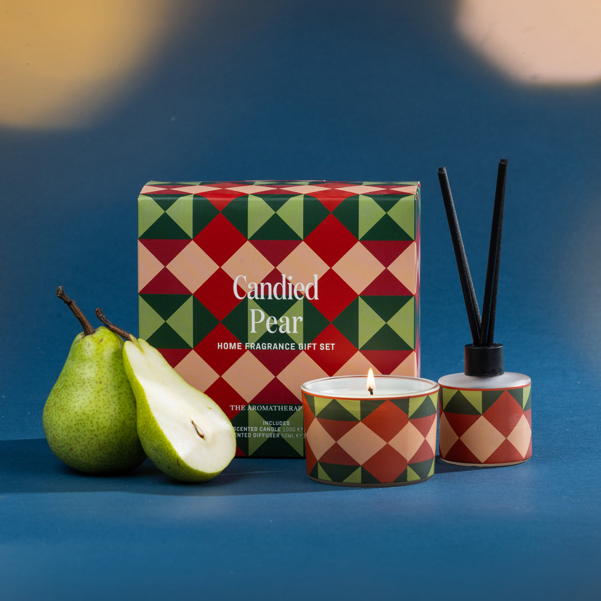 A festive Candied Pear home fragrance gift set featuring a coordinating candle and diffuser, styled with fresh pears against a rich blue backdrop.