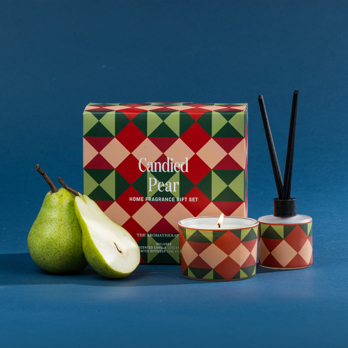A festive Candied Pear home fragrance gift set featuring a coordinating candle and diffuser, styled with fresh pears against a rich blue backdrop.