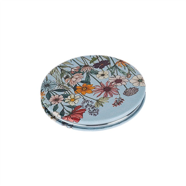 A round compact mirror with a light blue background and a dense, colorful wildflower pattern on the cover, shown against a plain white background.