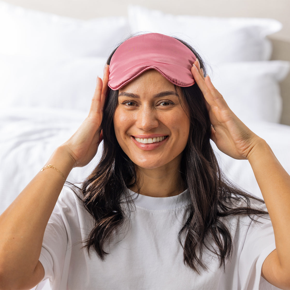 Woman wearing the Grace & Gild So Soft Pink Eye Mask in a bright bedroom setting.
