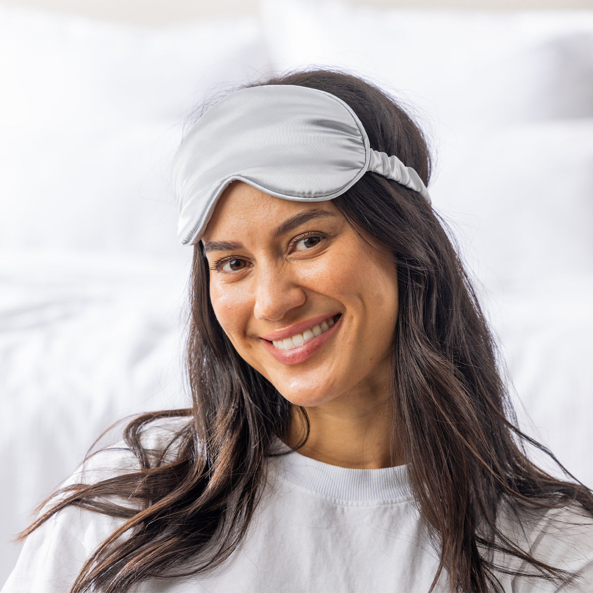 Woman wearing the Grace & Gild So Soft Silver Eye Mask in a bright bedroom setting.