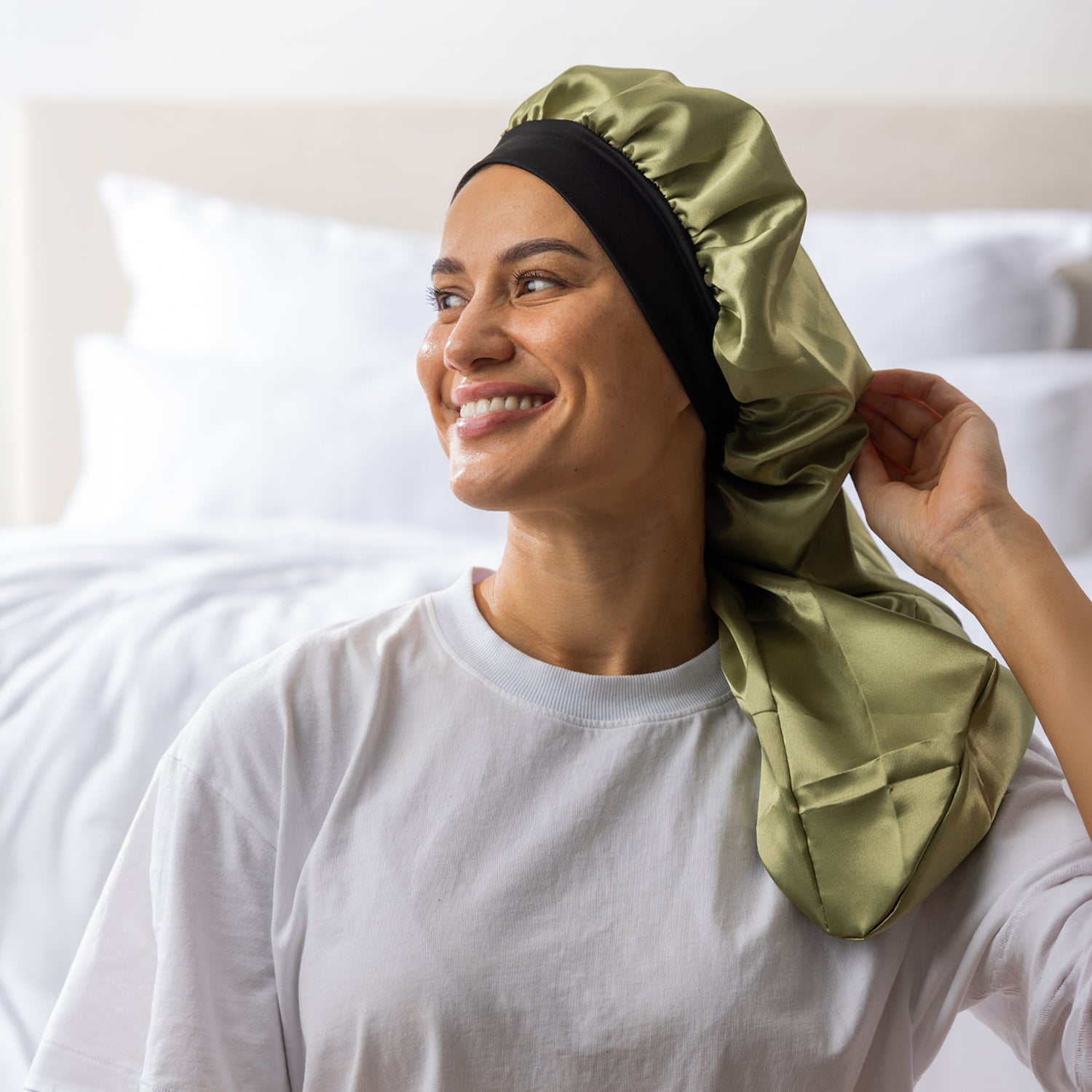 Woman adjusting the green Grace & Gild Long Sleep Bonnet with the long fabric section draped over her shoulder.