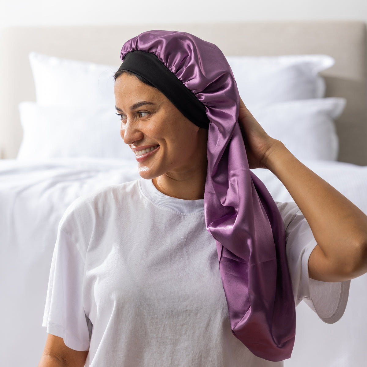 Woman adjusting the mauve Grace & Gild Long Sleep Bonnet with the long fabric section draped over her shoulder.