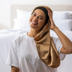 Woman adjusting the light brown Grace & Gild Long Sleep Bonnet with the long fabric section draped over her shoulder.