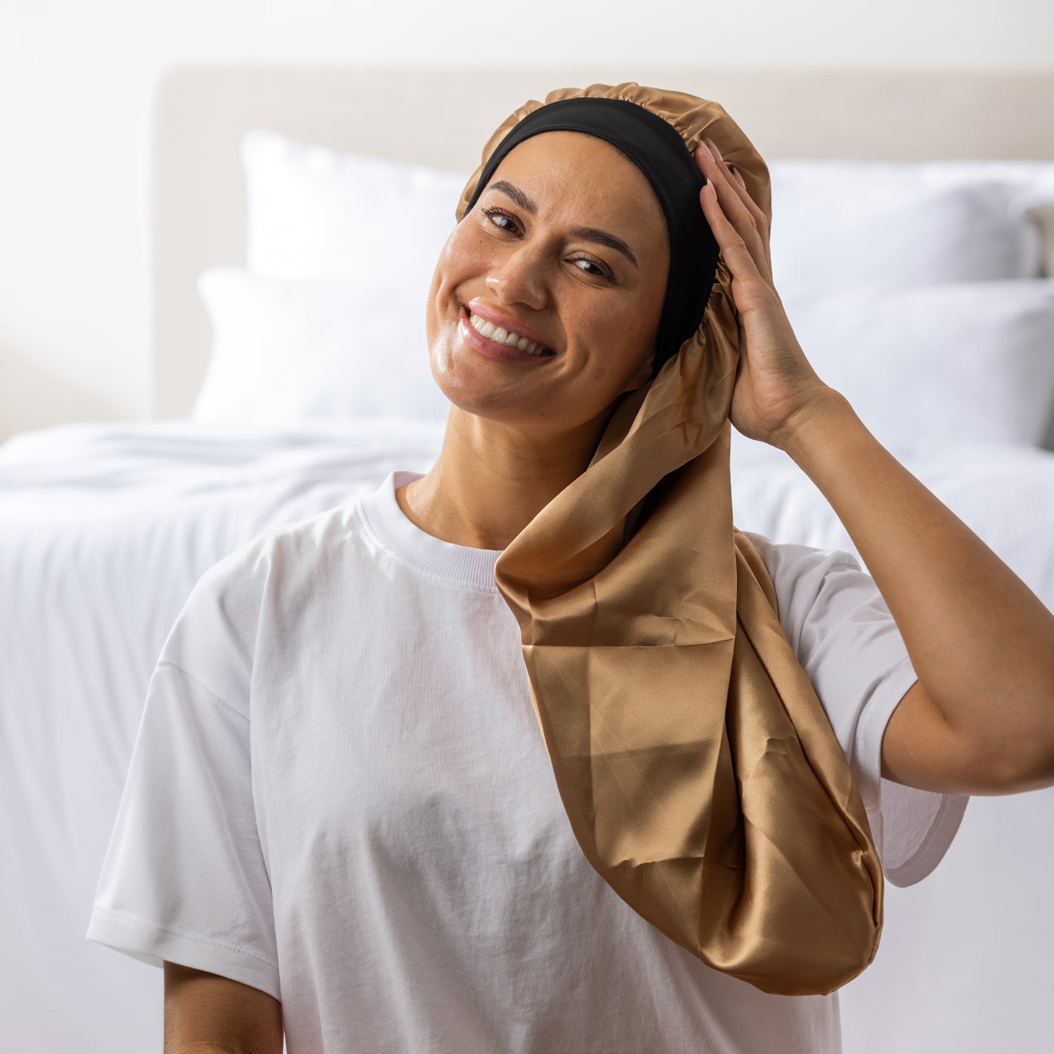 Woman adjusting the light brown Grace & Gild Long Sleep Bonnet with the long fabric section draped over her shoulder.