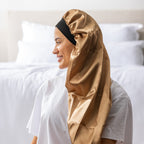 Side view of a woman wearing the light brown Grace & Gild Long Sleep Bonnet with a black band.