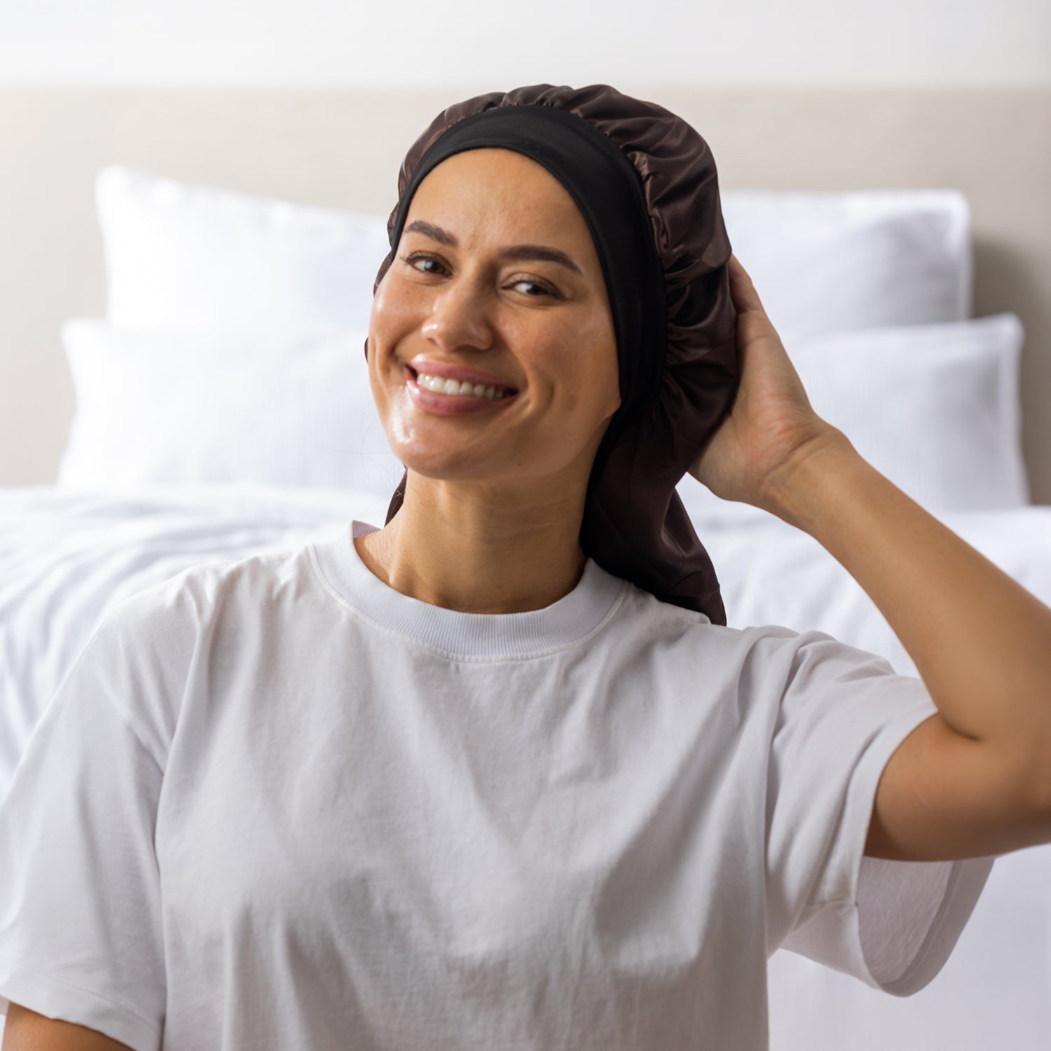 Woman adjusting the dark brown Grace & Gild Long Sleep Bonnet with a wide black band.