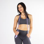 Woman holding a purple skipping rope around her shoulders while dressed in activewear.