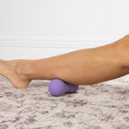 Purple textured massage ball positioned beneath the lower leg for targeted muscle massage and recovery.