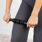 Woman using a black textured massage roller on her upper thigh as part of a fitness and recovery routine.
