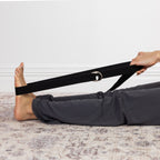 Woman using a black yoga strap behind her back to stretch her shoulders and upper body.