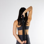 Woman using a black yoga strap behind her back to stretch her shoulders and upper body.