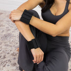 Woman wearing black weighted wrist bands while seated in activewear.