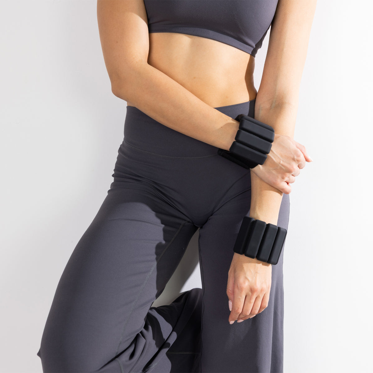 Woman wearing a pair of black weighted wrist bands as part of a strength and fitness routine.