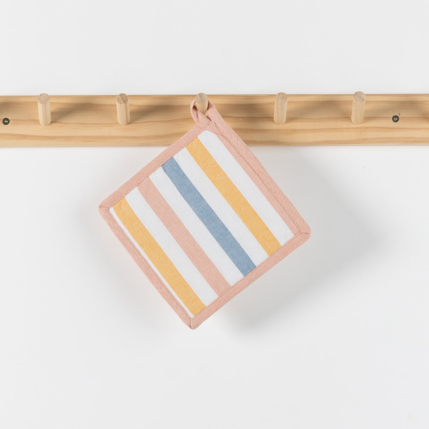 A square fabric potholder with pastel stripes in pink, yellow, blue, and white, hanging from a light wood peg rack against a white wall.