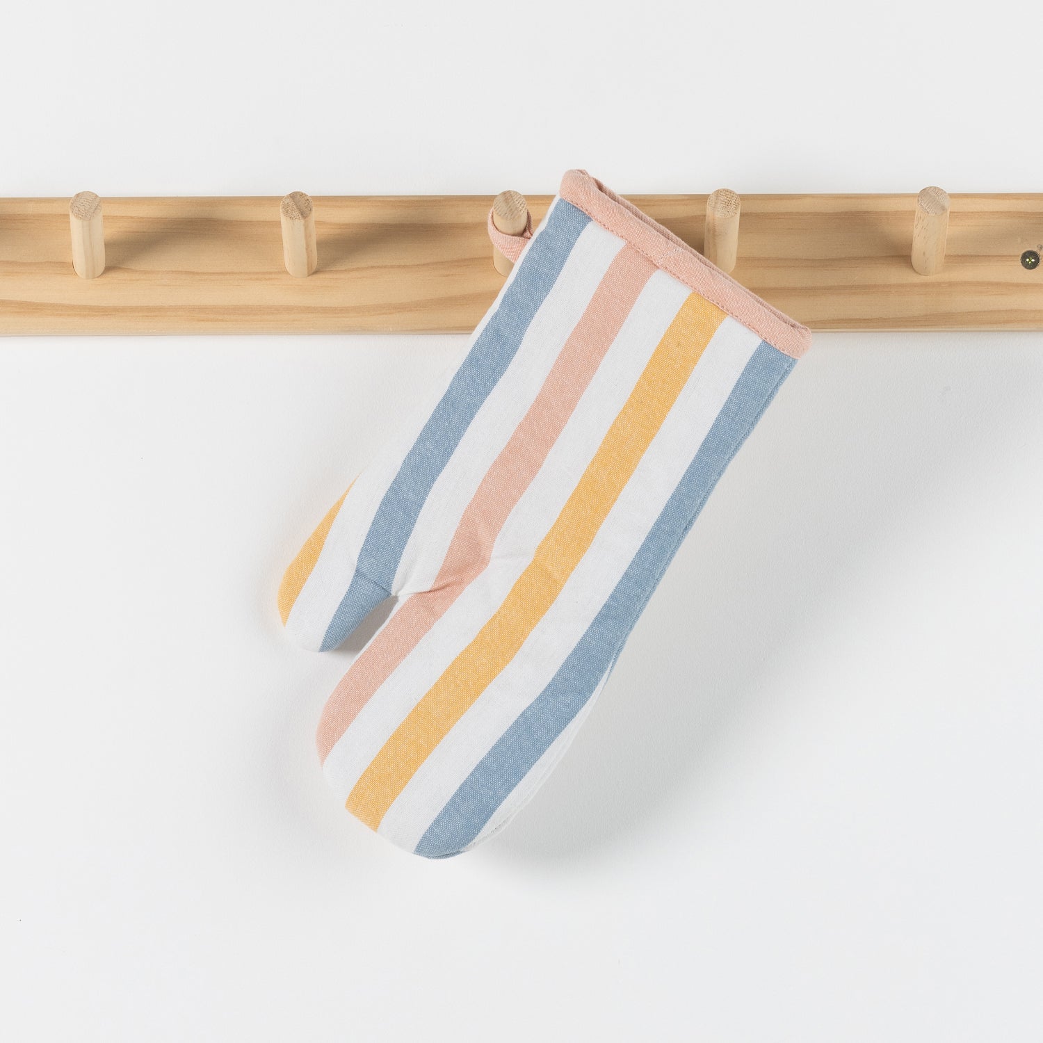 A striped oven mitt with vertical bands of dusty blue, peach pink, mustard yellow, and white, hanging from a light wood peg rack against a white wall.