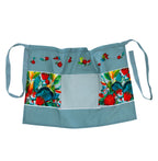 Design Plus Kiwiana Pohutukawa Half Apron featuring a soft sage green background with vibrant pōhutukawa floral panels, scattered floral motifs, a large front pocket and adjustable waist ties.