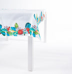 Design Plus Kiwiana Pohutukawa Tablecloth featuring a vibrant pōhutukawa floral border with rich green foliage on a crisp white tablecloth, draped over a white dining table in a clean studio setting.