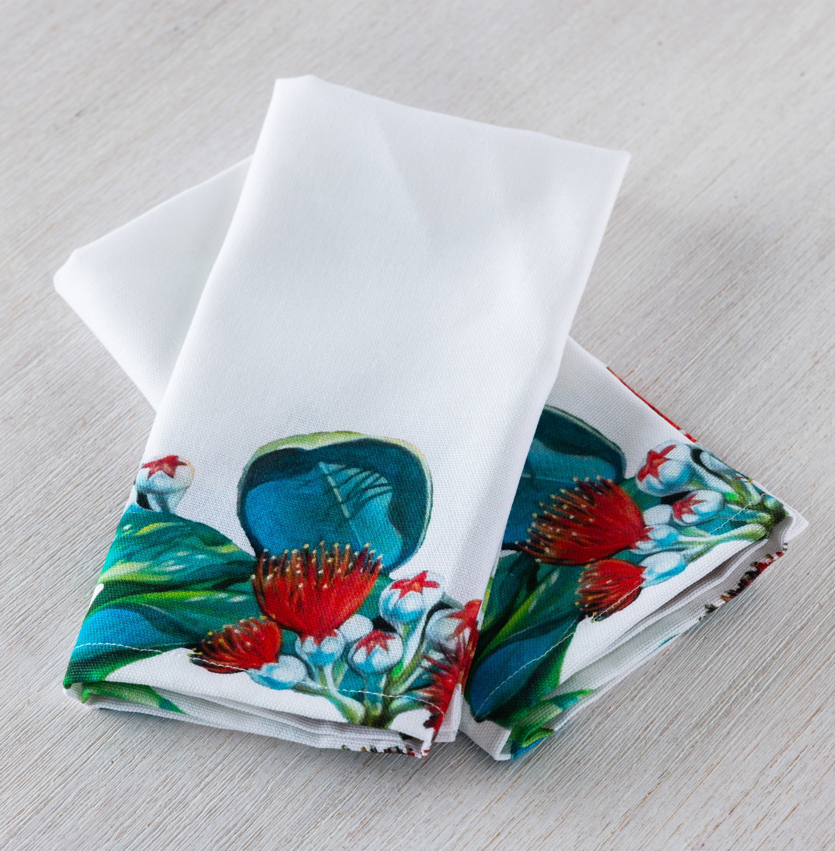 Design Plus Kiwiana Pohutukawa 2 Pack Napkins folded neatly to showcase the vibrant pōhutukawa floral border on a crisp white background.