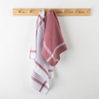 Two dishtowels hanging on a wooden rack against a white wall.