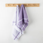 Purple and white checkered towels hanging on a wooden rack against a white wall.