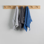 Three kitchen towels hanging from a light wood peg rack against a plain light coloured wall. 