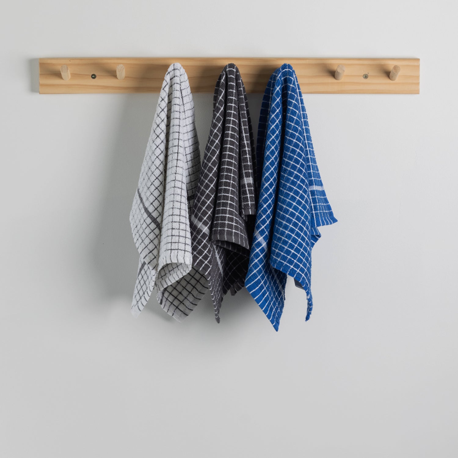 Three kitchen towels hanging from a light wood peg rack against a plain light coloured wall. 