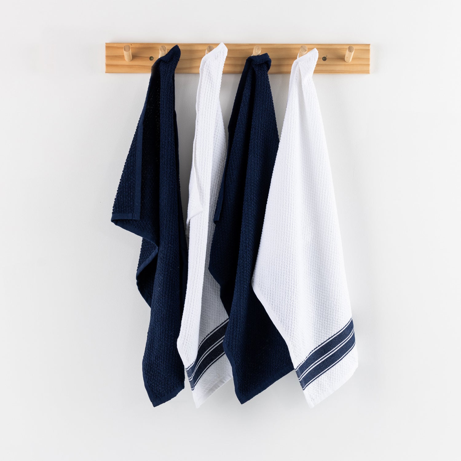 A set of four textured tea towels in alternating white and blue tones hangs neatly from a light timber wall rack, creating a clean and inviting kitchen display.