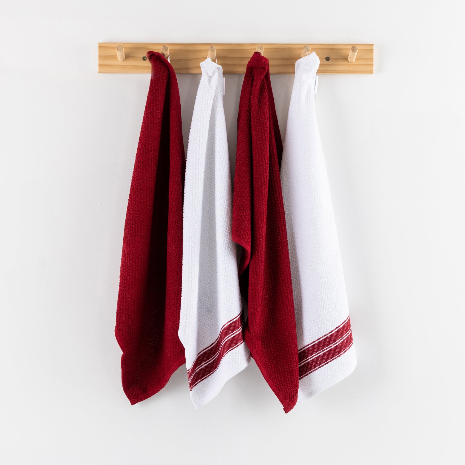 A set of four textured tea towels in alternating white and red tones hangs neatly from a light timber wall rack, creating a clean and inviting kitchen display.