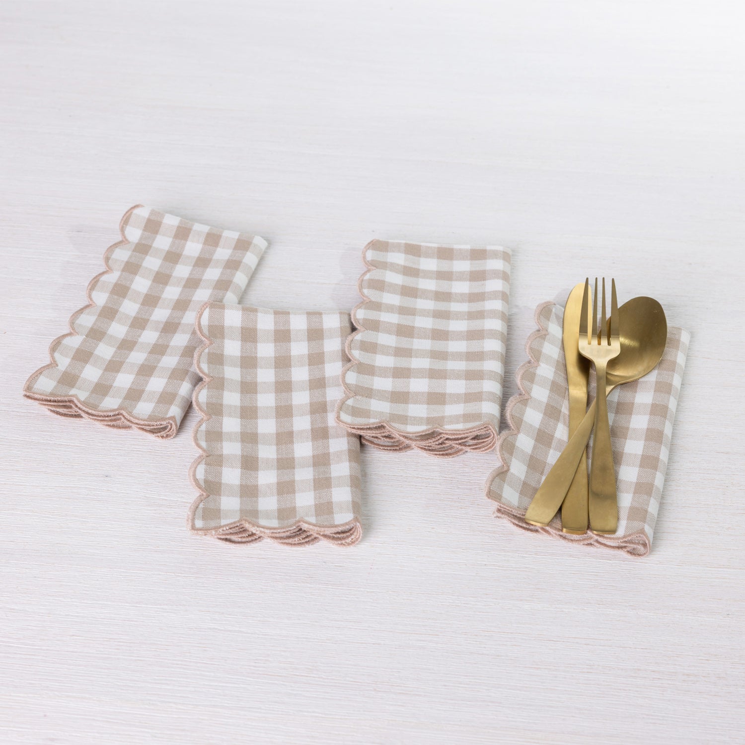 Gather Scallop Vichy Check napkin 4 pack in Brown/Cream arranged on a white table, with one napkin styled with gold-toned cutlery.