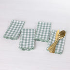 Gather Scallop Vichy Check napkin 4 pack in Green/Ivory arranged on a white table, with one napkin styled with gold-toned cutlery.