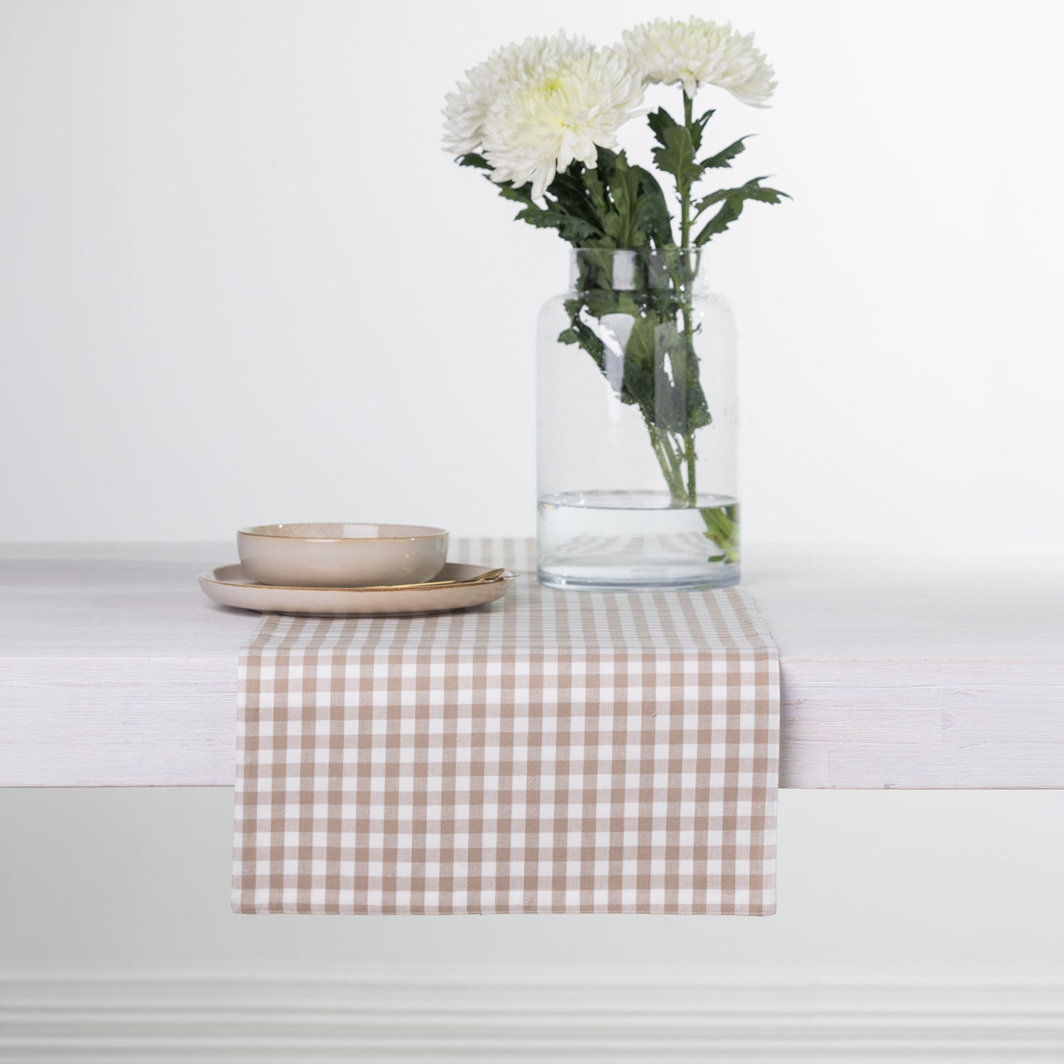 Gather Vichy Checks fused table runner in Brown/Cream styled with neutral dinnerware and a glass vase of white flowers.