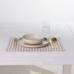 Gather Vichy Checks fused placemat in Brown/Cream styled with neutral dinnerware, gold-toned cutlery and a glass of water.