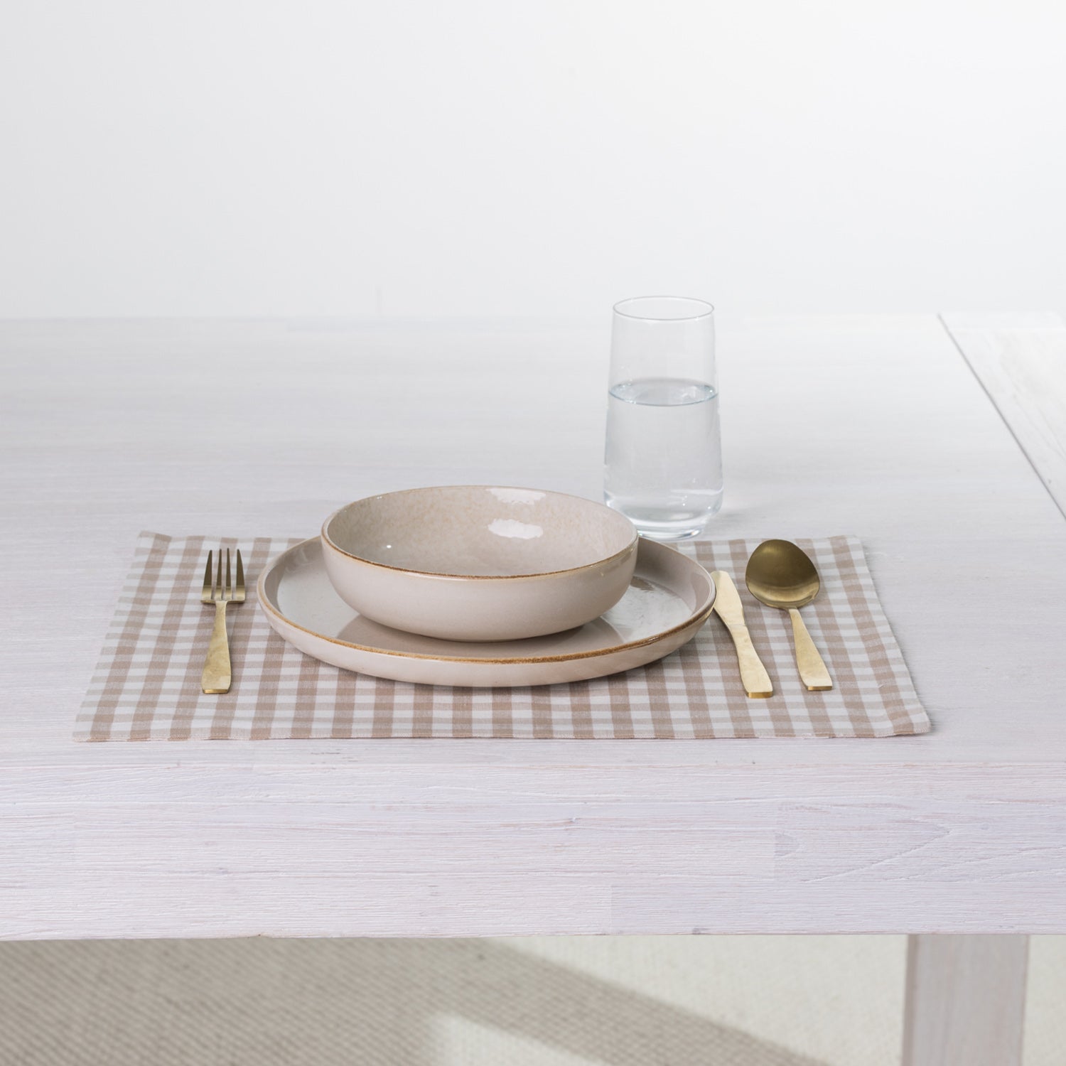 Gather Vichy Checks fused placemat in Brown/Cream styled with neutral dinnerware, gold-toned cutlery and a glass of water.