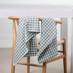 Gather Vichy Checks tea towels in Green/Ivory draped over the back of a wooden dining chair.