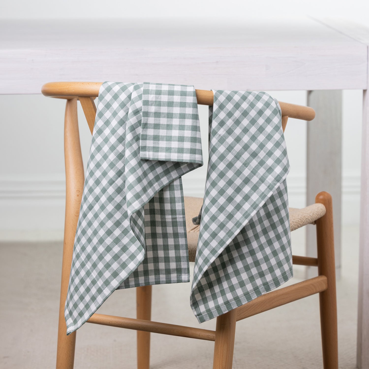 Gather Vichy Checks tea towels in Green/Ivory draped over the back of a wooden dining chair.
