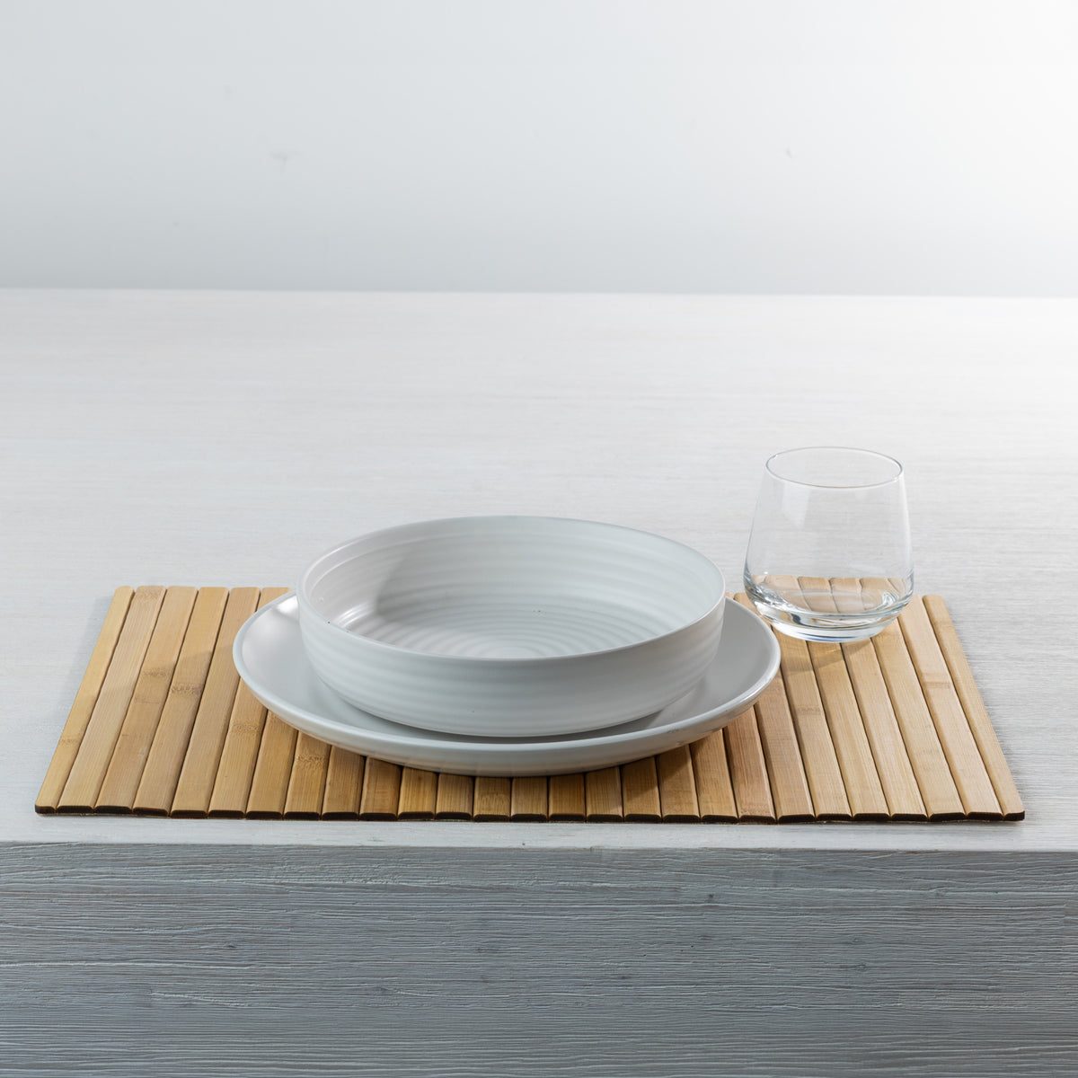 Gather Bamboo Placemat in Natural, displayed on a white dining table with a white ceramic bowl, matching plate and clear drinking glass.
