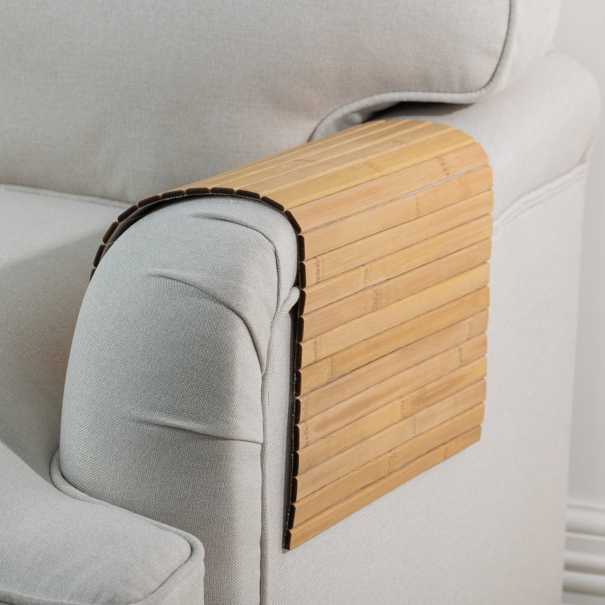 Gather Bamboo Armchair Mat in Natural, featuring smooth bamboo slats draped over the armrest of a light beige upholstered armchair.