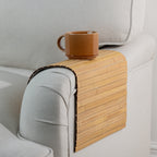 Gather Bamboo Armchair Mat in Natural, featuring a flexible slatted bamboo design curved over a beige armchair armrest with a brown ceramic mug on top.