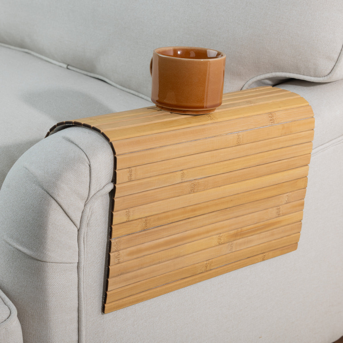 Gather Bamboo Armchair Mat in Natural, styled over a beige armchair with a brown ceramic mug resting on top, showcasing its practical design.