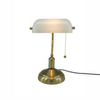 A classic brass desk lamp with a white glass shade, illuminated, on a solid white background.