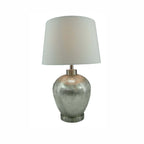 A table lamp with a textured, metallic silver base and a tapered off-white fabric drum shade, set against a plain white background.