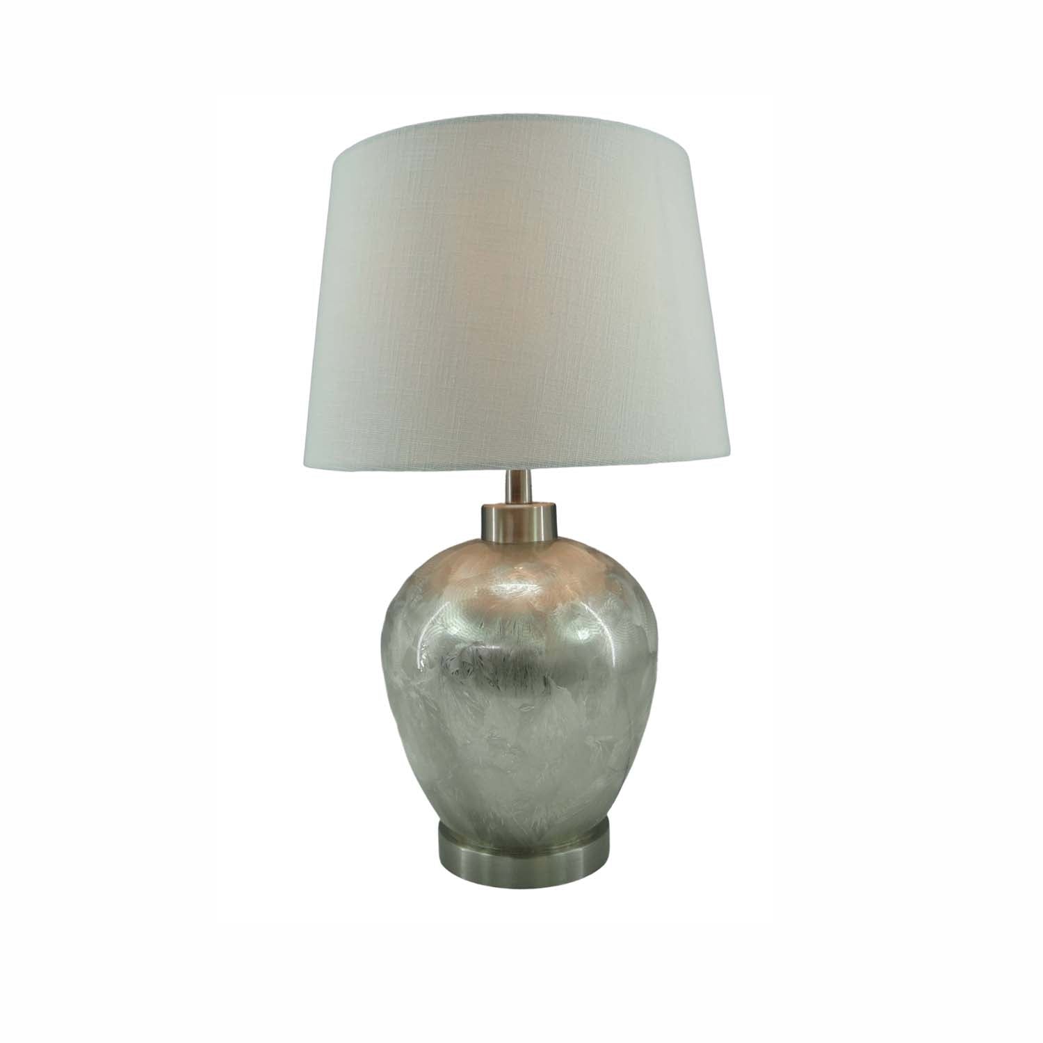 A table lamp with a textured, metallic silver base and a tapered off-white fabric drum shade, set against a plain white background.