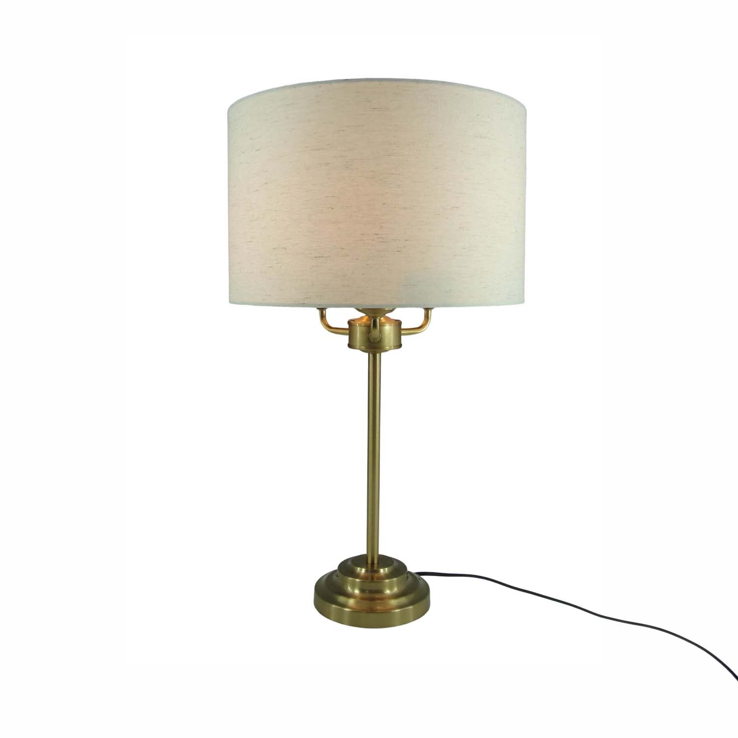 A table lamp with a cylindrical off-white fabric shade and a brass-finished metal base and stem, shown on a plain white background with its power cord visible.