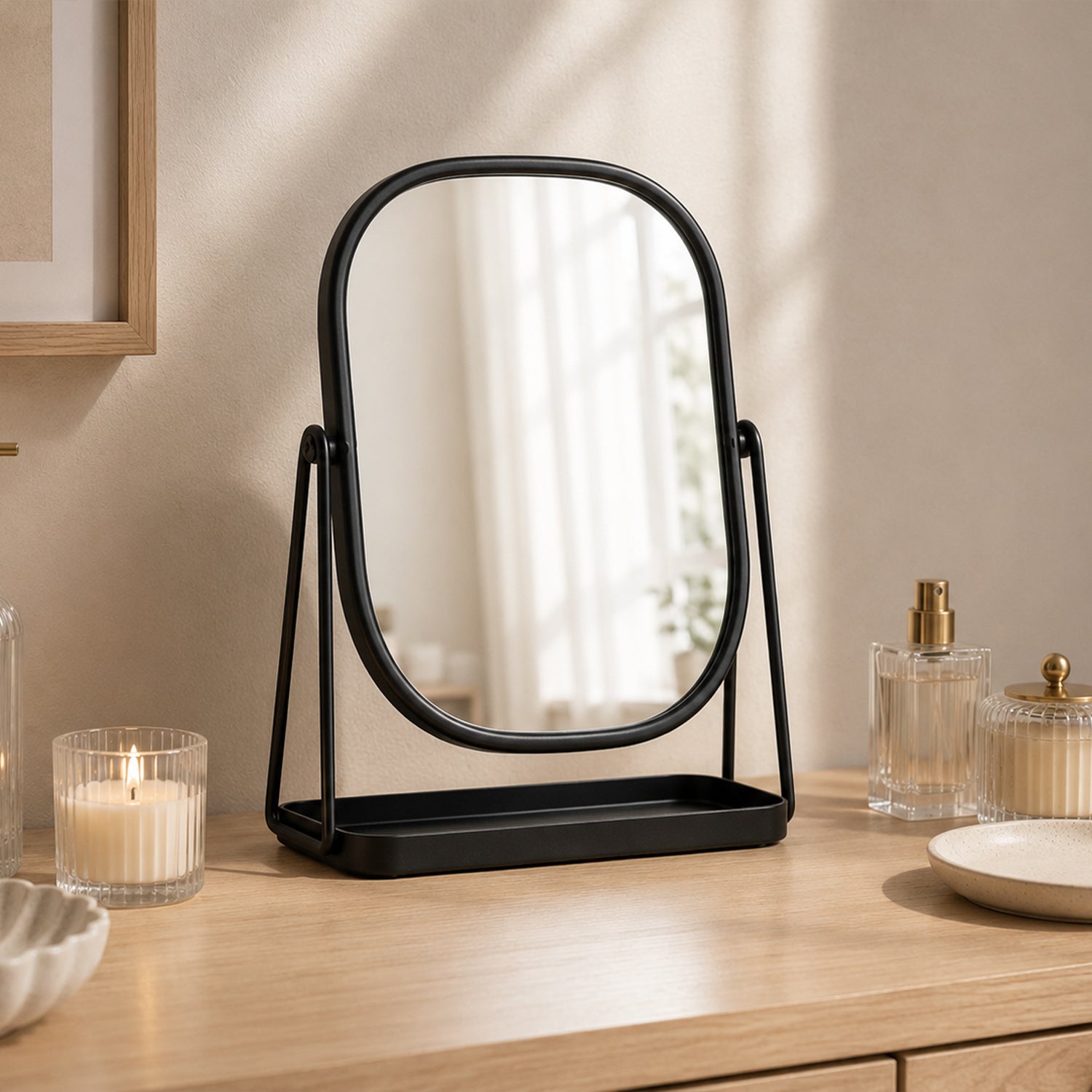 Black tabletop vanity mirror with a rounded rectangular frame displayed on a wooden vanity with candles, perfume bottles, and decorative accessories.