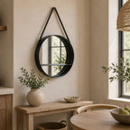 Round black hanging wall mirror with an integrated shelf displayed above a wooden console table in a modern neutral interior.