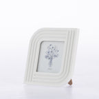 A white ceramic picture frame with a rounded, ribbed border and a small wooden stand, featuring a blue line-art illustration of a flower bouquet on the insert.